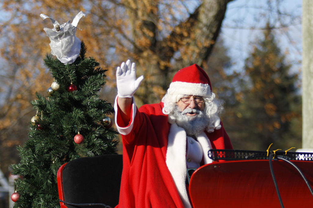 Santa on his sled riding into town and waving at the people.