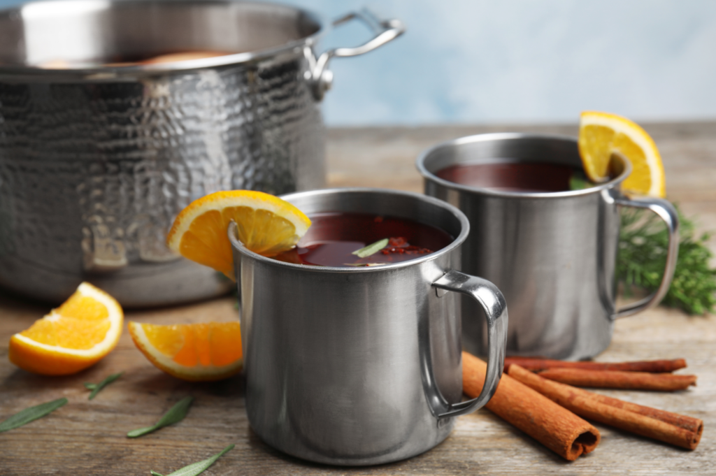 Two tin cups filled with wassail with lemon and cinnamon.